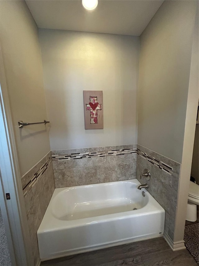 bathroom with wood finished floors, a garden tub, toilet, and tile walls