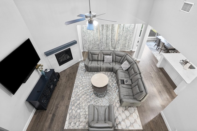 living room featuring ceiling fan, a glass covered fireplace, baseboards, wood finished floors, and visible vents