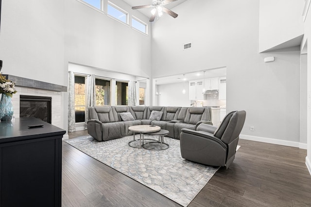 living room featuring ceiling fan, a high ceiling, dark wood-style flooring, and visible vents