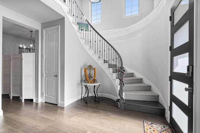 staircase with an inviting chandelier, baseboards, a towering ceiling, and wood finished floors