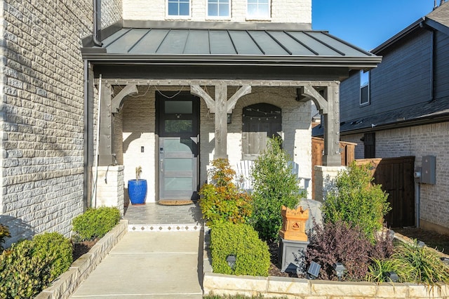 doorway to property featuring a standing seam roof, covered porch, metal roof, and brick siding