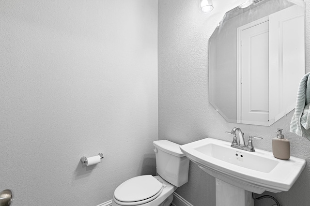 bathroom featuring baseboards, a sink, a textured wall, and toilet