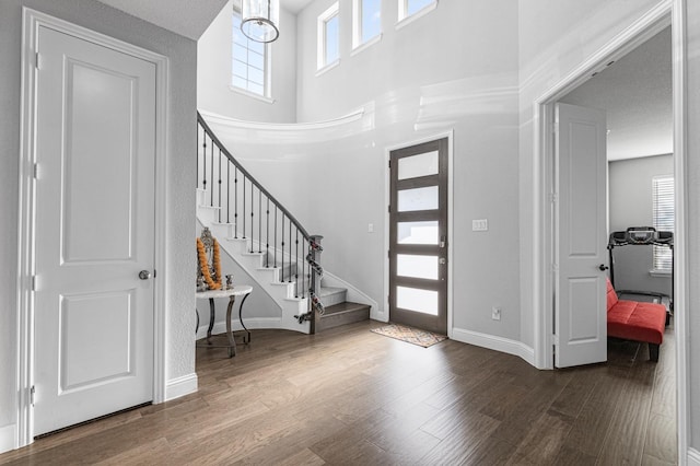 foyer featuring baseboards, wood finished floors, stairway, and a towering ceiling