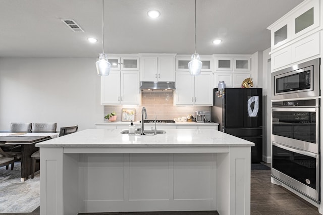 kitchen featuring visible vents, a kitchen island with sink, under cabinet range hood, a sink, and stainless steel appliances