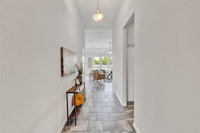 hall featuring a textured wall and baseboards