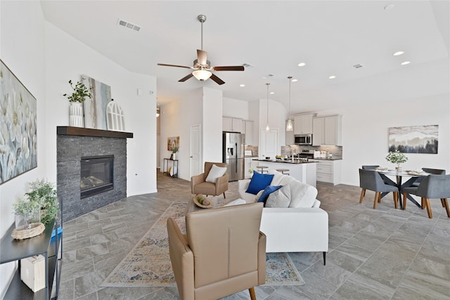 living area with a stone fireplace, visible vents, recessed lighting, and ceiling fan