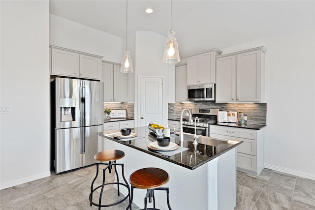 kitchen with an island with sink, a breakfast bar area, stainless steel appliances, backsplash, and baseboards