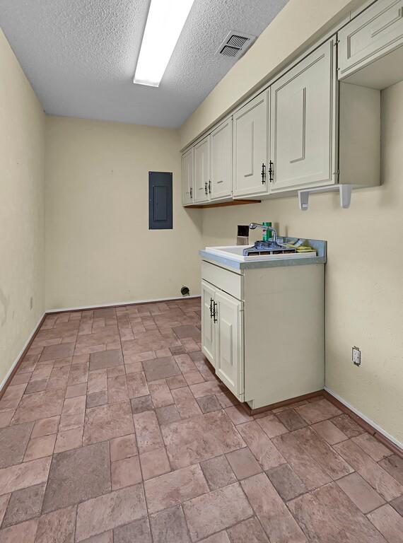 laundry room with a textured ceiling, electric panel, visible vents, a sink, and baseboards