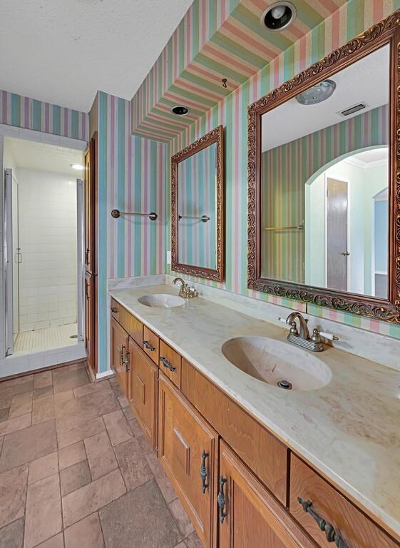 bathroom with wallpapered walls, double vanity, a sink, and visible vents