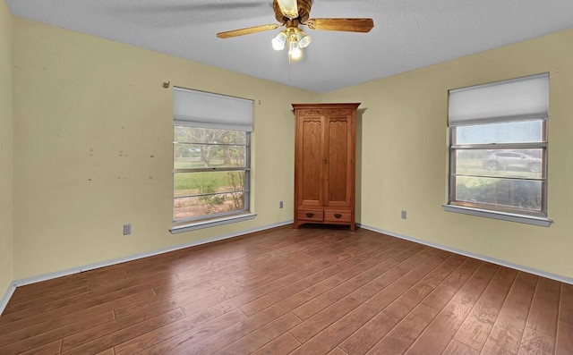 spare room featuring dark wood-type flooring, ceiling fan, baseboards, and a wealth of natural light