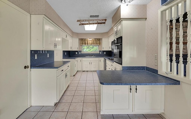 kitchen with black appliances, a peninsula, wallpapered walls, and dark countertops