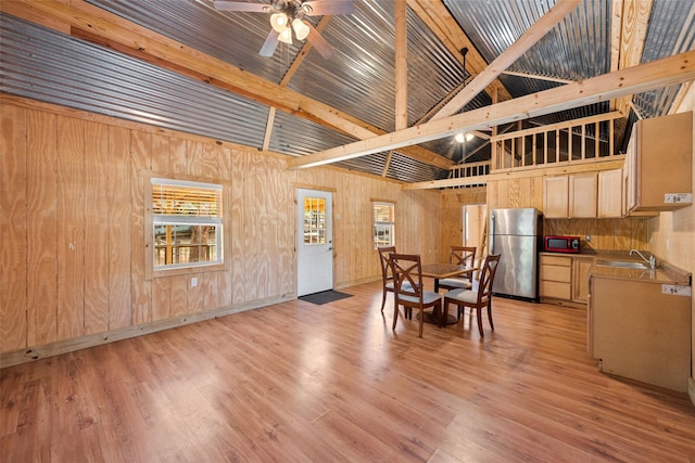 dining area featuring light wood-style flooring, wood walls, high vaulted ceiling, and ceiling fan