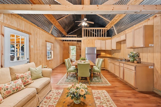 dining space with light wood finished floors, ceiling fan, wood walls, and beamed ceiling