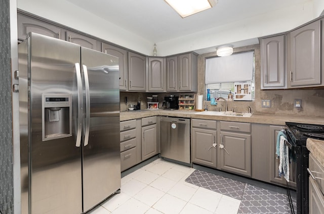 kitchen with gray cabinets, light countertops, decorative backsplash, stainless steel appliances, and a sink