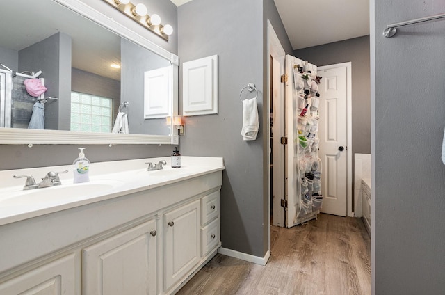 bathroom with a sink, baseboards, double vanity, and wood finished floors