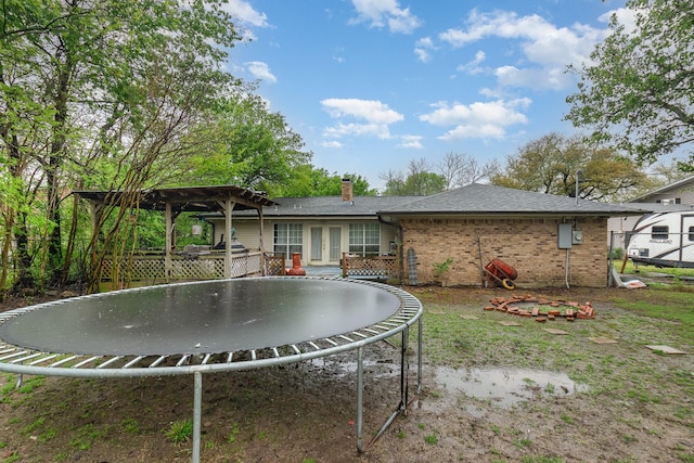 back of property with a pergola, a trampoline, a chimney, brick siding, and french doors