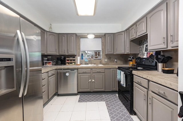 kitchen with a sink, gray cabinets, light countertops, and appliances with stainless steel finishes
