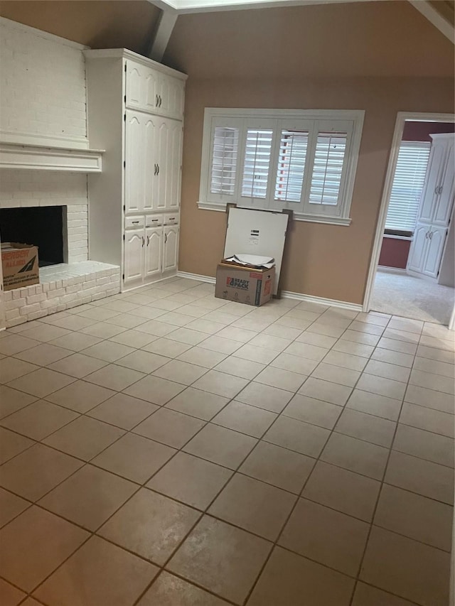 unfurnished living room featuring baseboards, lofted ceiling, light tile patterned flooring, and a fireplace