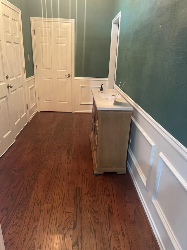 hall featuring dark wood-style floors, wainscoting, and a decorative wall