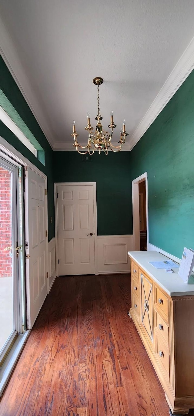 unfurnished dining area featuring crown molding, a chandelier, wainscoting, and wood finished floors