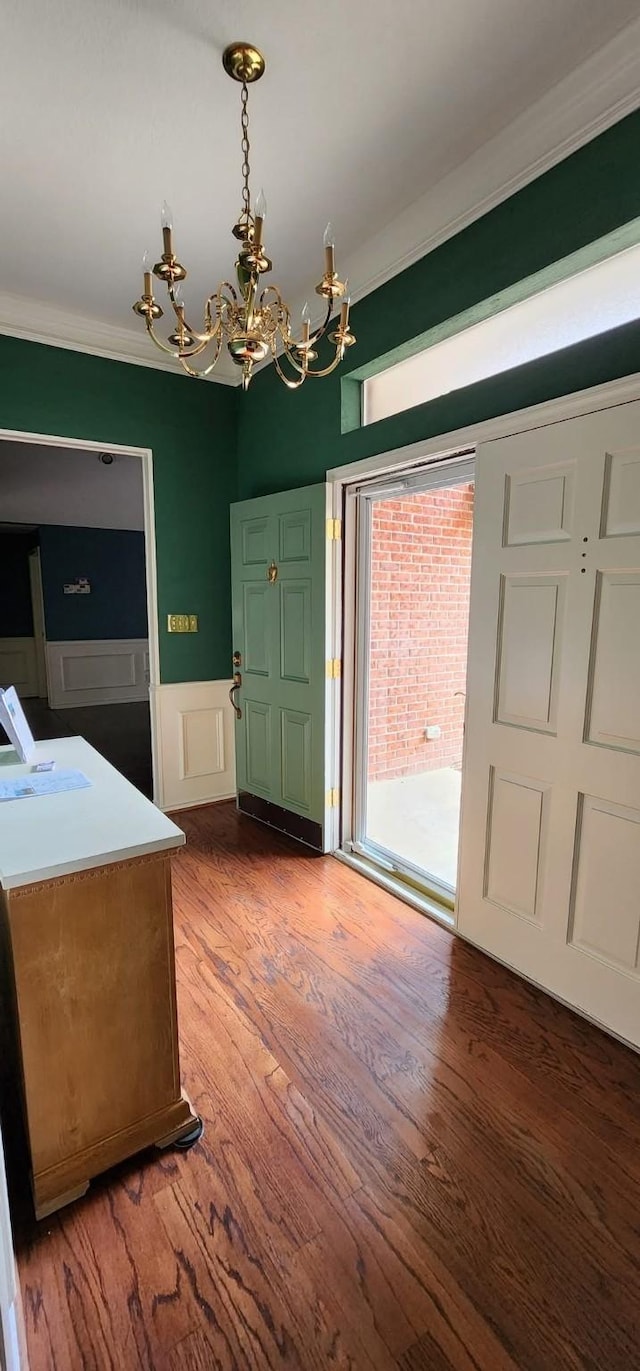 entryway featuring a notable chandelier, wainscoting, a decorative wall, wood finished floors, and ornamental molding