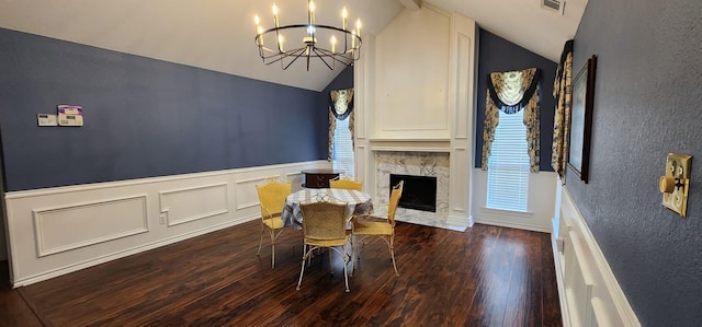 dining area featuring an inviting chandelier, a fireplace, a wainscoted wall, wood finished floors, and vaulted ceiling