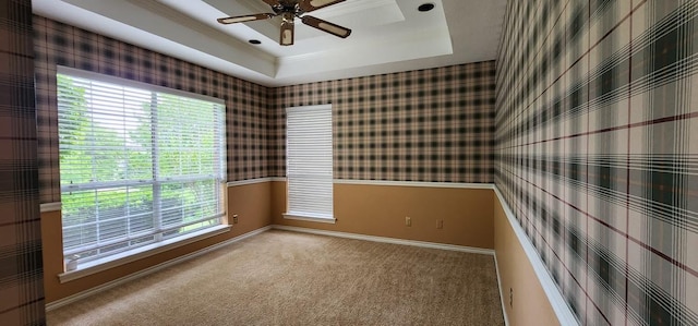 empty room featuring carpet flooring, a tray ceiling, plenty of natural light, and ceiling fan