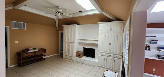 living area with vaulted ceiling with skylight, a ceiling fan, visible vents, a brick fireplace, and light tile patterned flooring