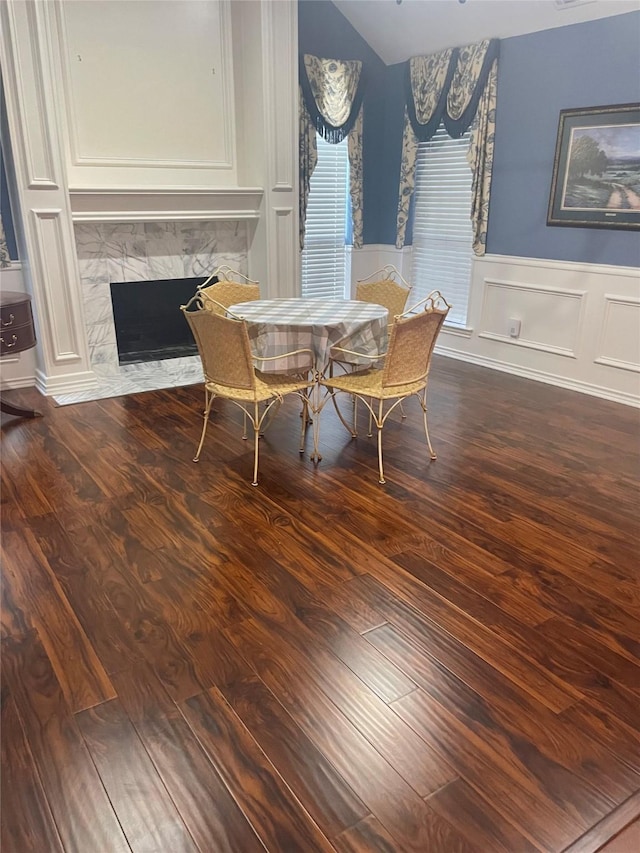 dining area featuring dark wood-style flooring, a decorative wall, a wainscoted wall, and a premium fireplace