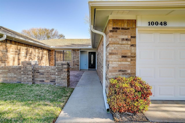 doorway to property with a garage, a shingled roof, and brick siding