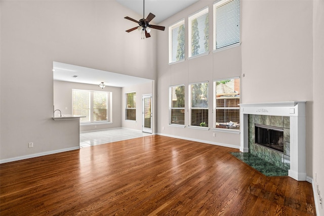 5921 Colby Dr, Plano, TX 75094 - unfurnished living room featuring wood finished floors, ceiling fan, a towering ceiling, and a tile fireplace