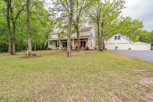 view of front of home with a front yard, a shingled roof, a detached garage, covered porch, and an outdoor structure
