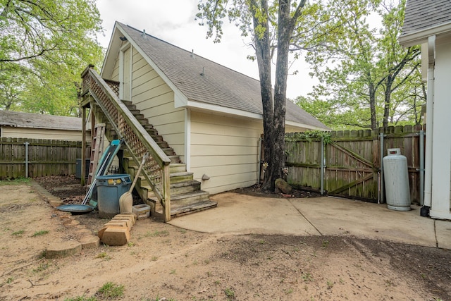 back of property with stairway, roof with shingles, a patio, fence, and a gate