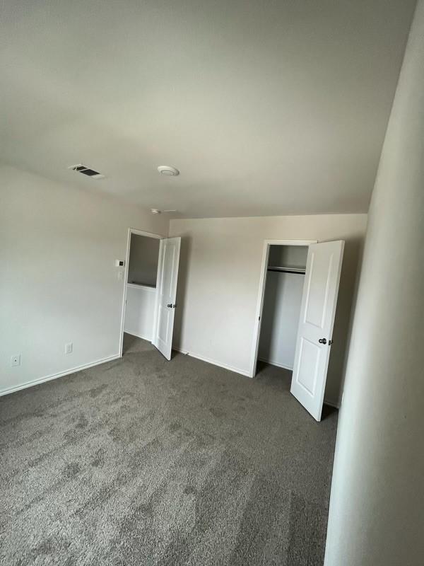 unfurnished bedroom featuring visible vents, baseboards, and dark carpet