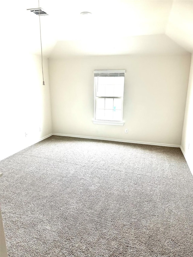 carpeted spare room featuring visible vents, baseboards, and lofted ceiling
