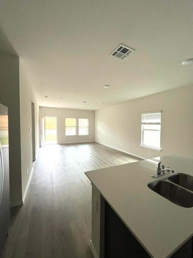 kitchen with baseboards, stainless steel refrigerator, visible vents, a sink, and wood finished floors