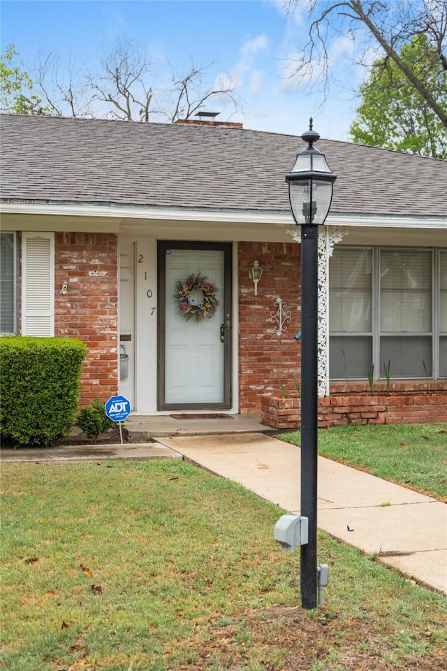 2107 Elizabeth Dr, Brownwood, TX 76801 - view of exterior entry with a yard, a shingled roof, and brick siding