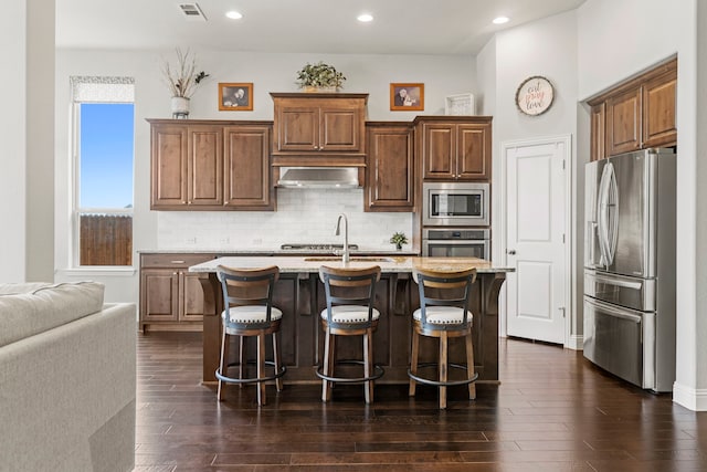 1036 Wedgewood Dr, Forney, TX 75126 - kitchen featuring stainless steel appliances, a breakfast bar area, decorative backsplash, a kitchen island with sink, and exhaust hood