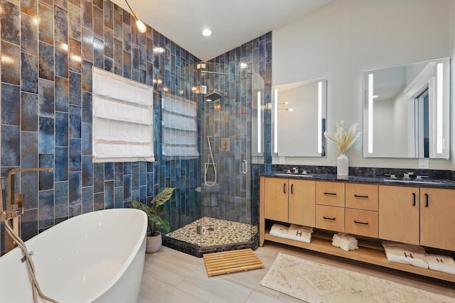 bathroom with double vanity, a stall shower, a freestanding bath, tile walls, and a sink