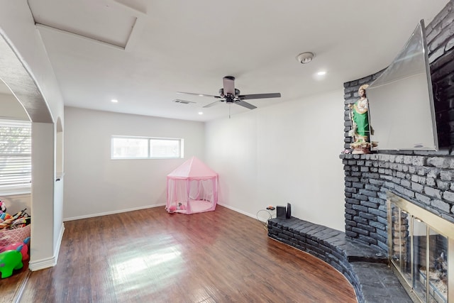 game room featuring a ceiling fan, visible vents, wood finished floors, a brick fireplace, and baseboards