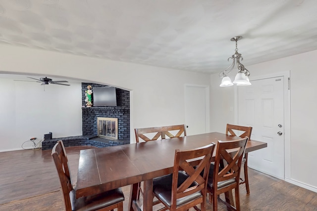 dining area featuring wood finished floors, ceiling fan, a fireplace, and baseboards