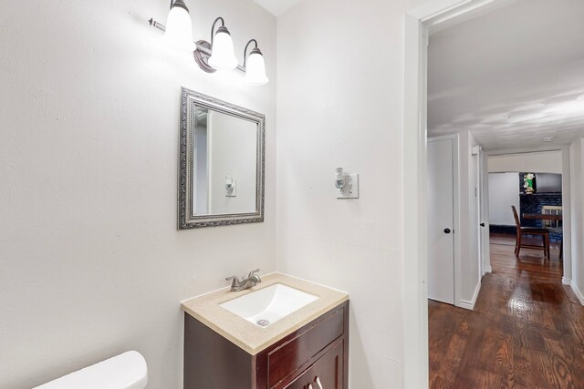 half bathroom with toilet, vanity, and wood finished floors