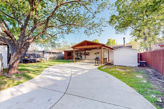 ranch-style house with a shed, a trampoline, a fenced backyard, an outdoor structure, and a patio