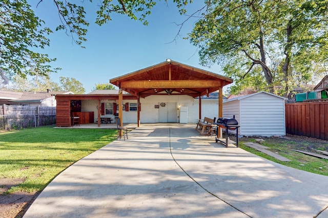 exterior space featuring an outdoor structure, a lawn, a patio, fence, and concrete driveway