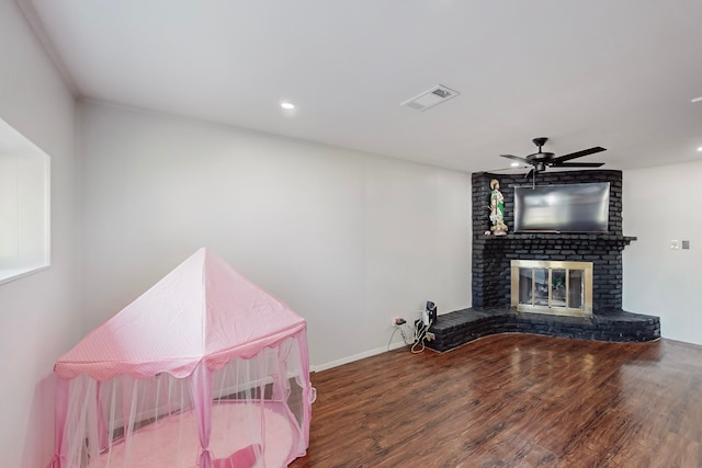 interior space featuring ceiling fan, a fireplace, visible vents, wood finished floors, and baseboards