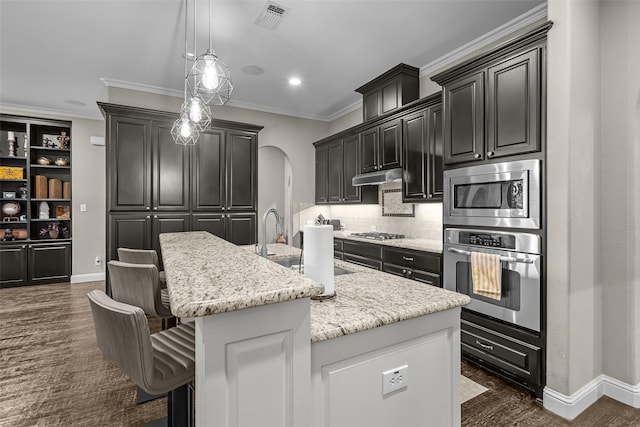 429 S Hampton Ct, Lewisville, TX 75056 - kitchen with under cabinet range hood, visible vents, a center island with sink, stainless steel appliances, and arched walkways