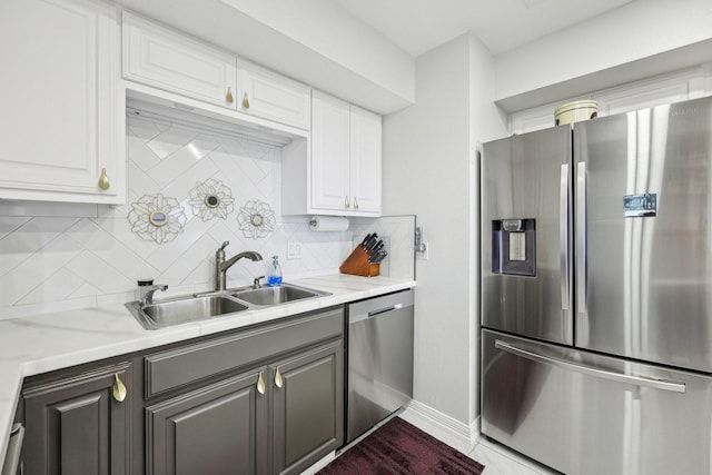 kitchen with a sink, stainless steel appliances, white cabinets, baseboards, and tasteful backsplash