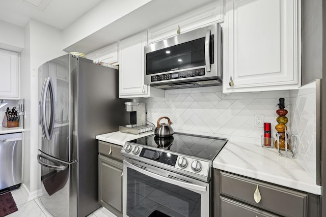 kitchen featuring light stone counters, white cabinetry, backsplash, gray cabinetry, and appliances with stainless steel finishes