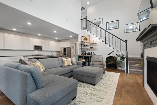 living area with a towering ceiling, recessed lighting, dark wood-style floors, stairs, and visible vents