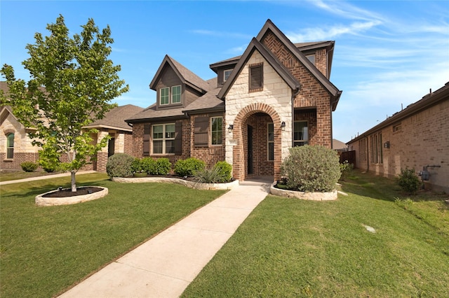 tudor home featuring a front yard, stone siding, and brick siding